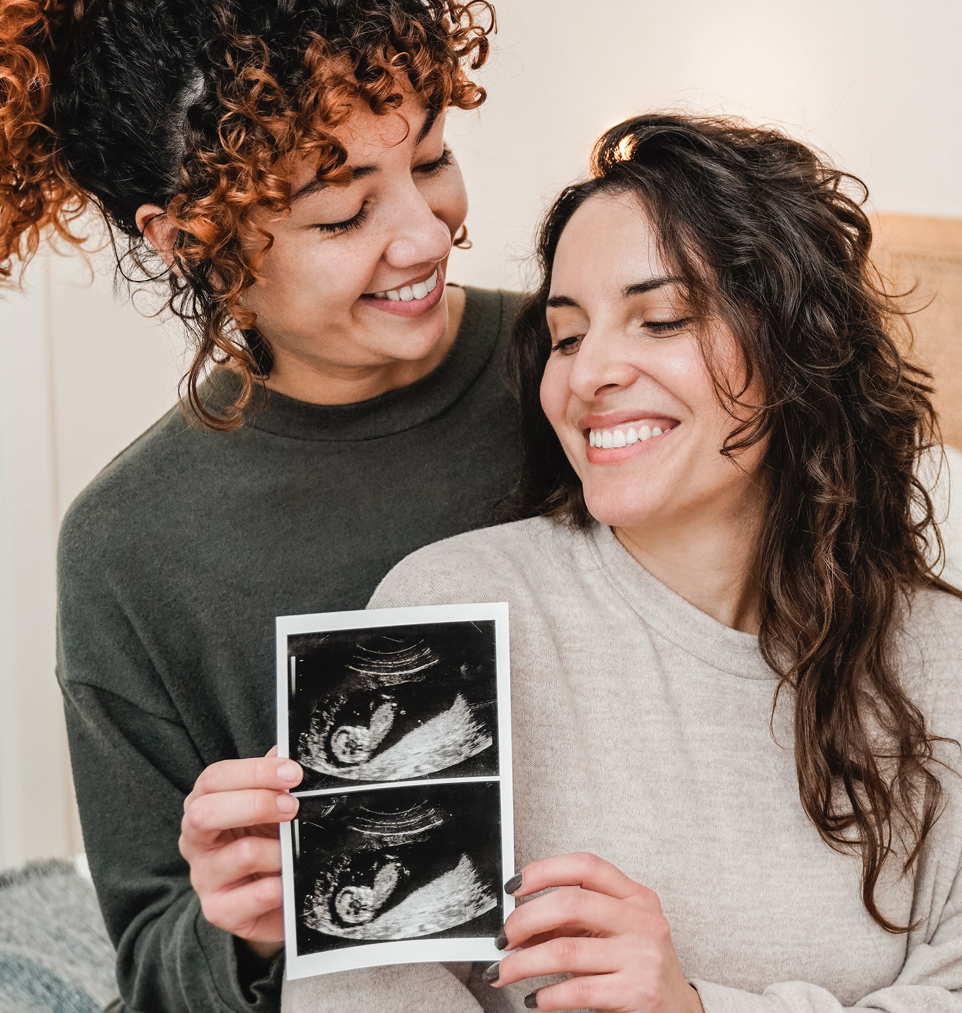 Female couple holding pictures of their baby's scan.